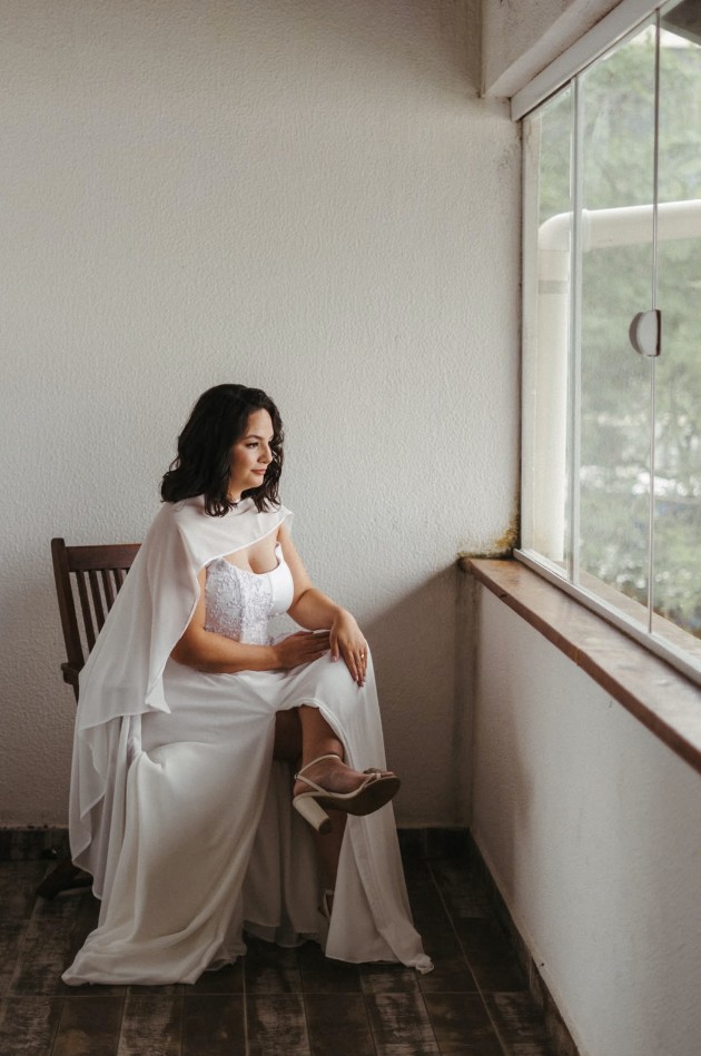 Modelo sentada com vestido longo branco e capa esvoaçante