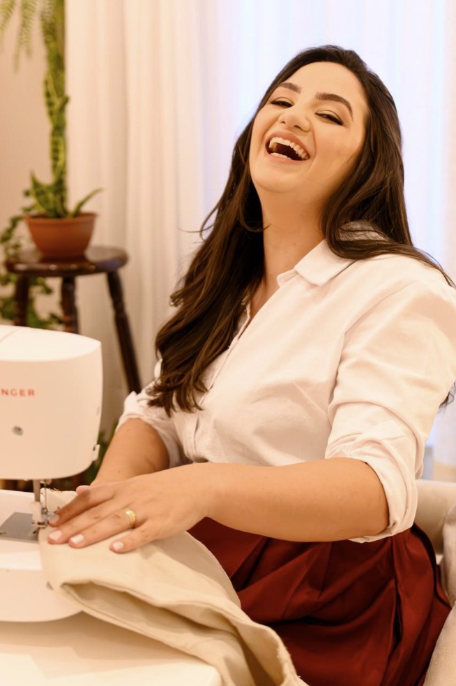 A costureira rindo diante da máquina de costura, com tecido nas mãos